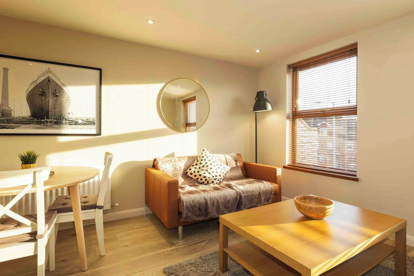 Una sala de estar moderna con una mesa de centro de madera, un sofá con cojines estampados, un espejo redondo y un cuadro en la pared.
