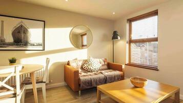 Una sala de estar moderna con una mesa de centro de madera, un sofá con cojines estampados, un espejo redondo y un cuadro en la pared.