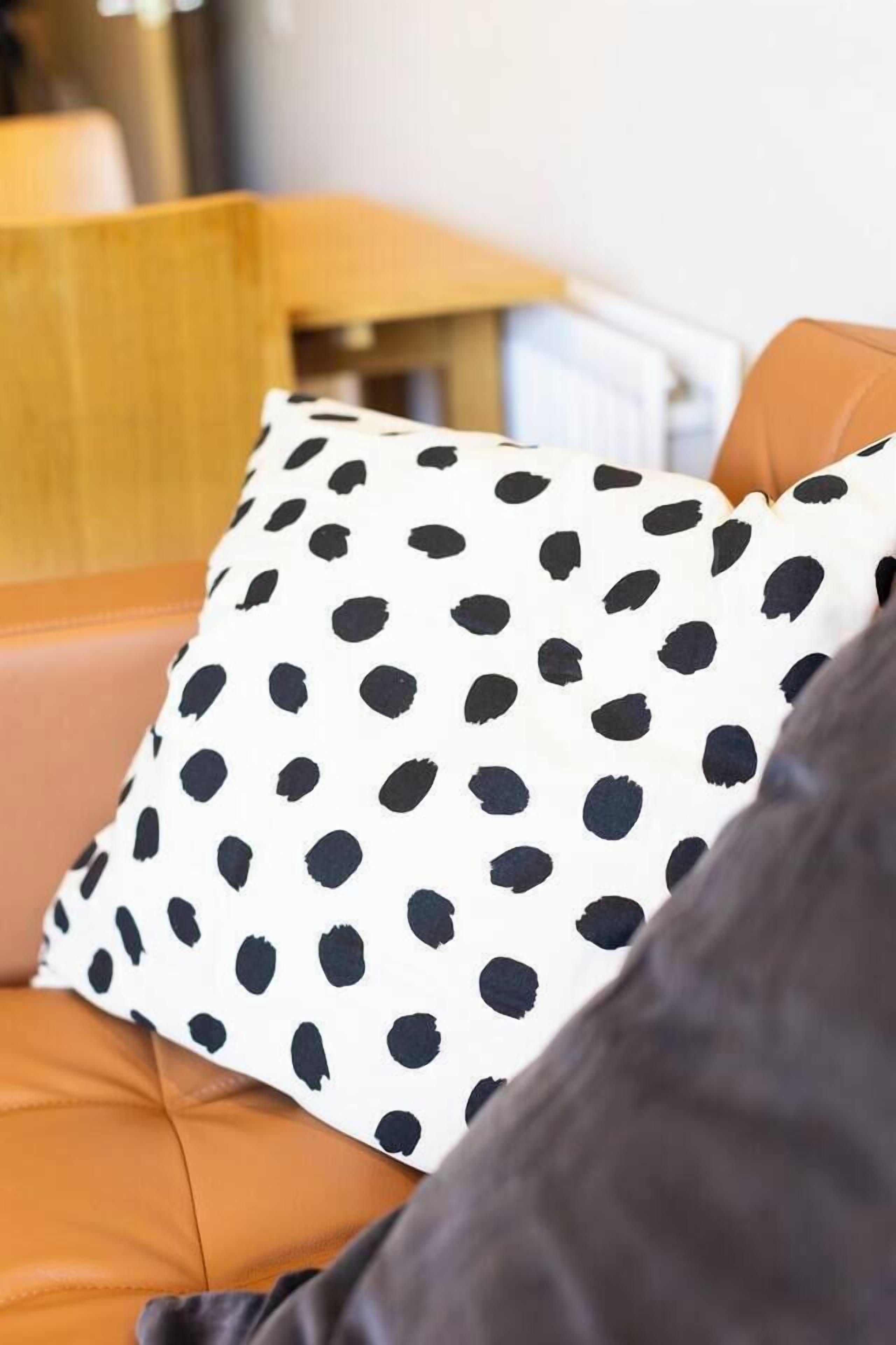 A close-up of a polka-dotted pillow on a brown leather couch.