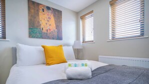 A hotel room with a large bed, a painting on the wall, and two windows with blinds. - The Manhattan -1bd City Ap (Gold Short Term Stays) (Belfast)