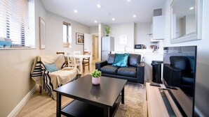A modern living room with a sofa, a coffee table, and a dining area with a table and chairs. - The Manhattan -1bd City Ap (Gold Short Term Stays) (Belfast)
