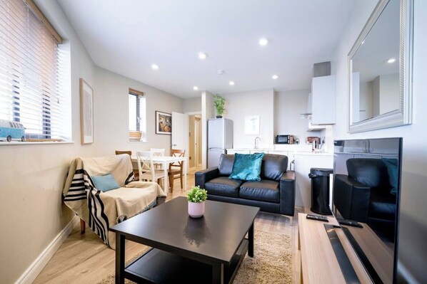 A modern living room with a sofa, a coffee table, and a dining area with a table and chairs. - The Manhattan -1bd City Ap (Gold Short Term Stays) (Belfast)