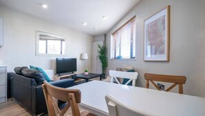 A modern living room with a sofa, TV, dining table, and chairs. - The Manhattan -1bd City Ap (Gold Short Term Stays) (Belfast)