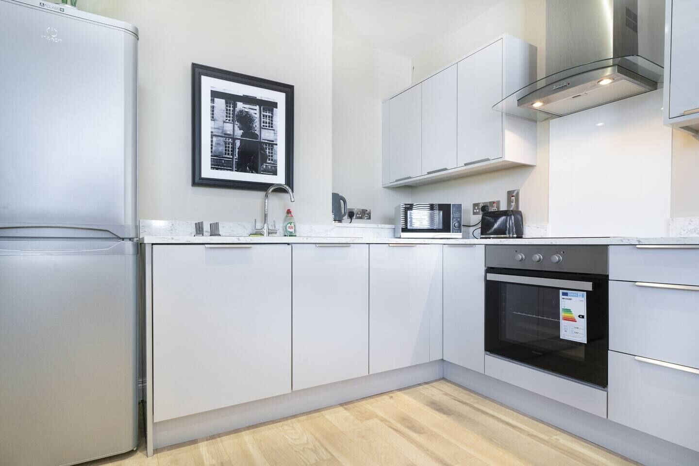 A modern kitchen with white cabinets, a stainless steel refrigerator, a microwave, a toaster, and an oven.