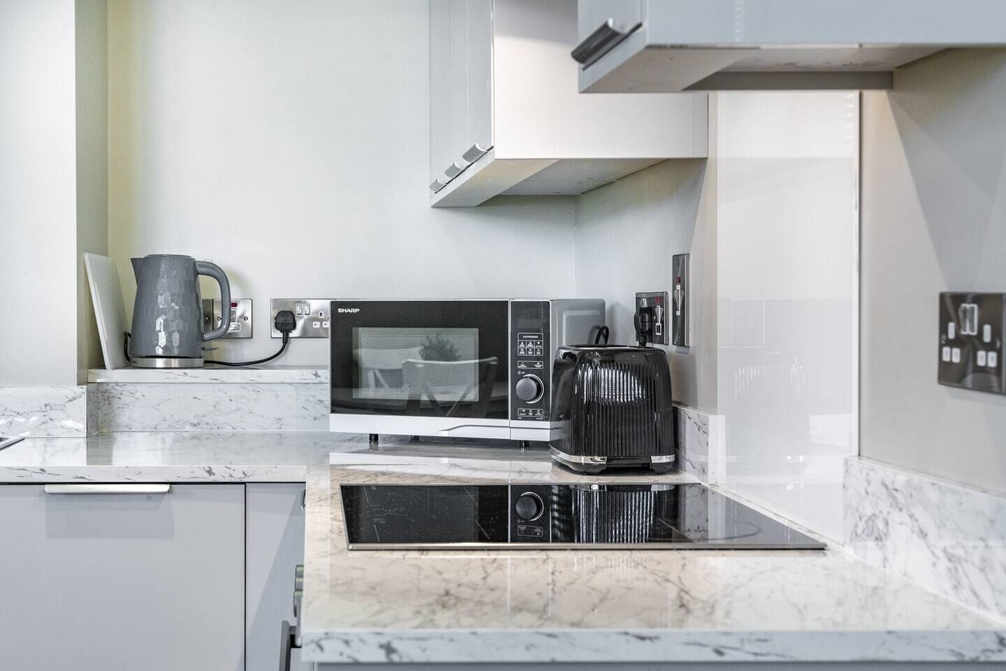 Una cocina moderna con microondas, tostadora y hervidor sobre una encimera de mármol.