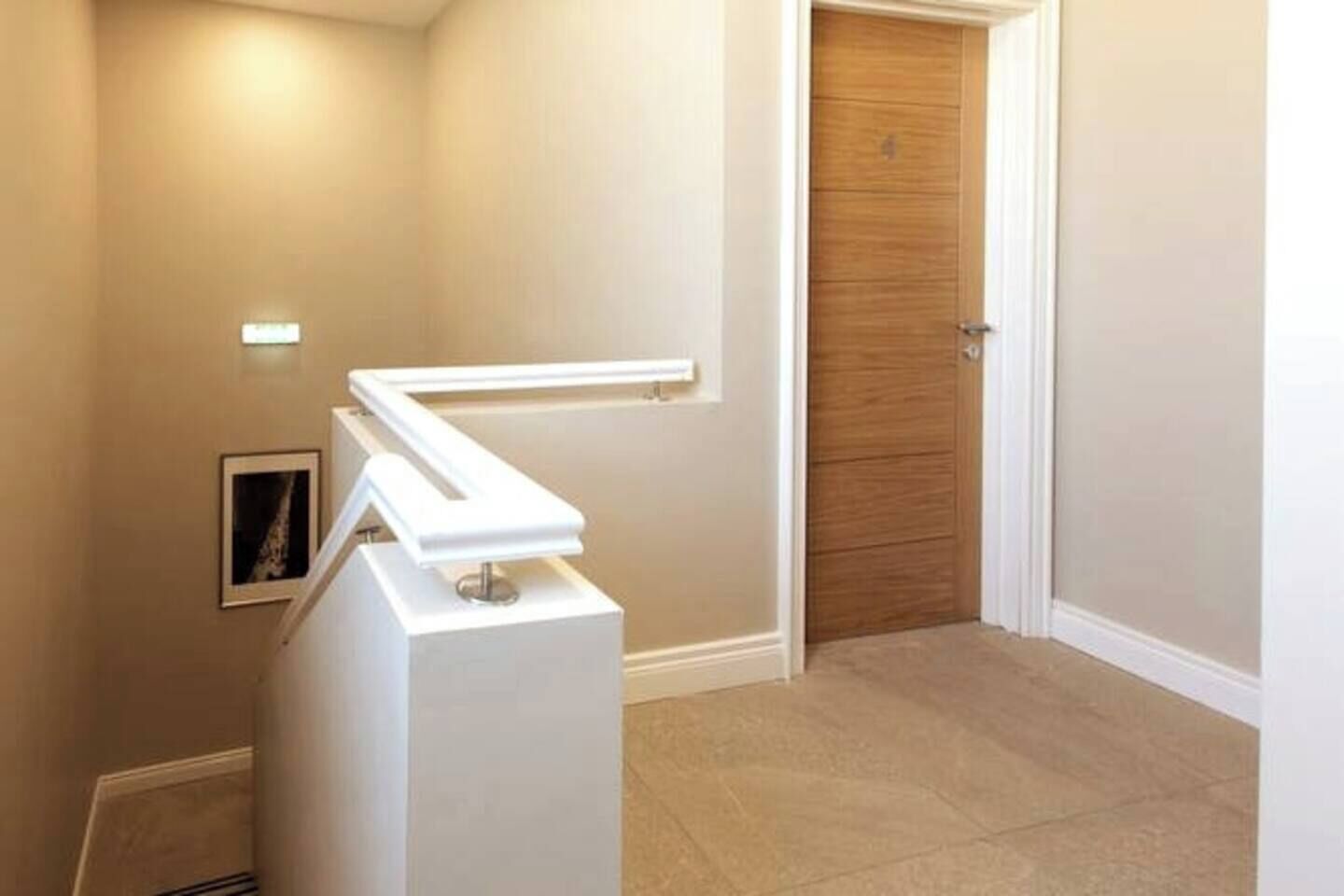 Un couloir avec un luminaire blanc fixé au mur, une porte en bois et un sol carrelé.