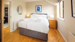 Ein Schlafzimmer mit einem großen Bett, einem Nachttisch, einem Spiegel und einem gerahmten Bild an der Wand.