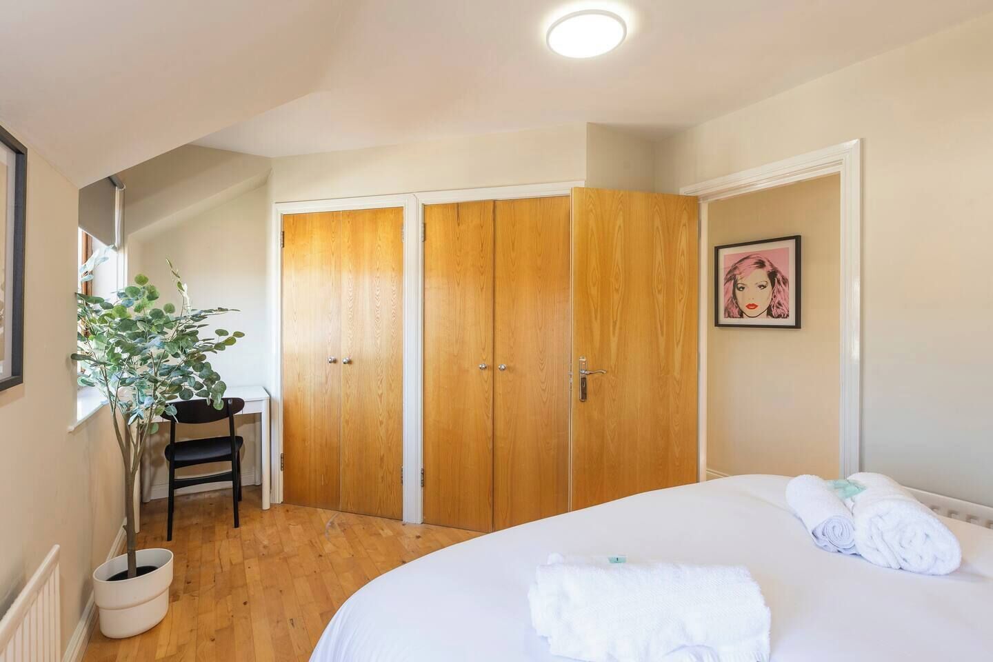 Une chambre à coucher avec un lit, un bureau, une plante en pot et une armoire.