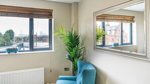 Ein Zimmer mit zwei Fenstern, einem Heizkörper, einem blauen Sessel und einem großen Spiegel.