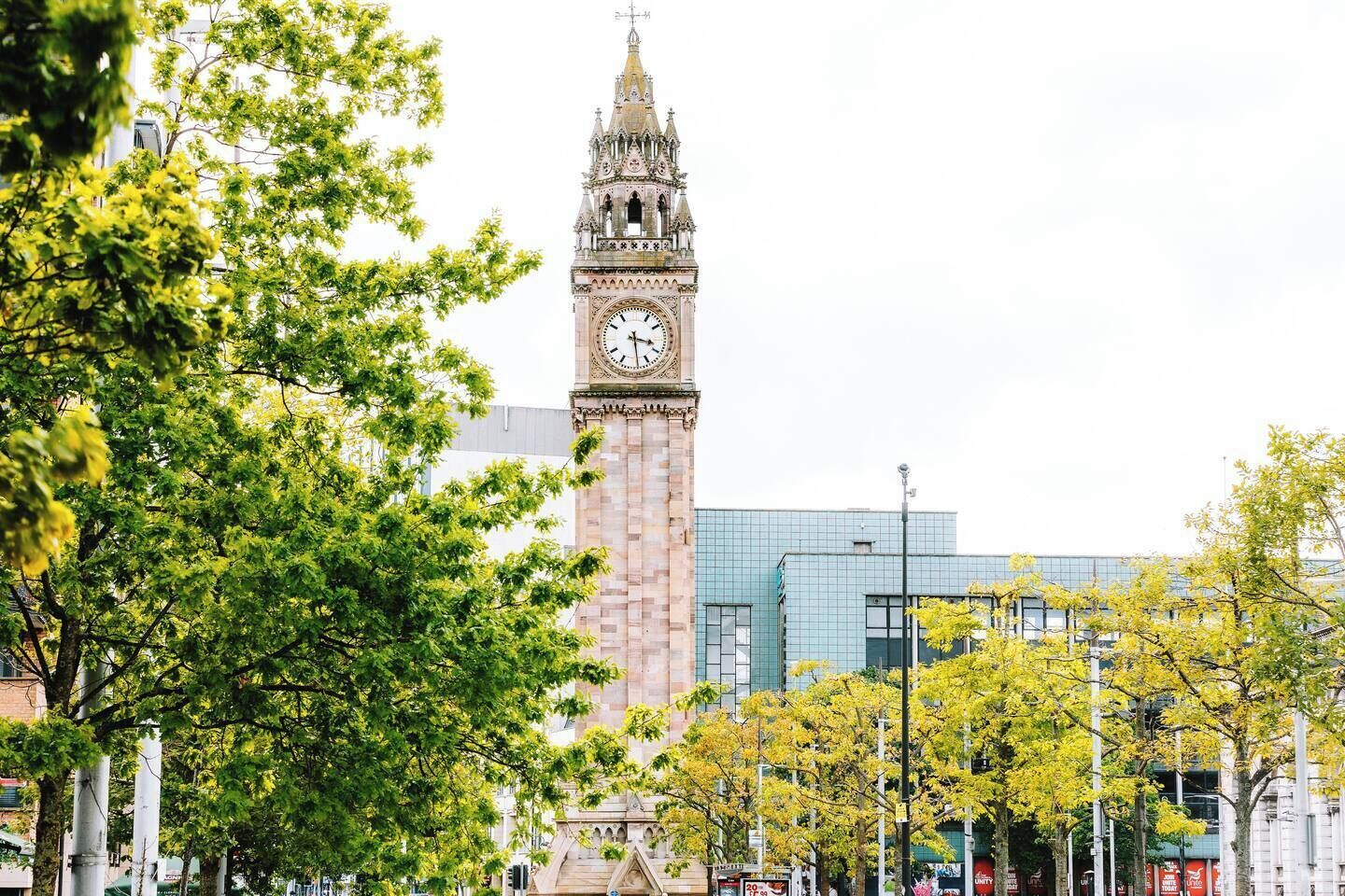 A clock tower with a clock face, surrounded by trees and modern buildings.