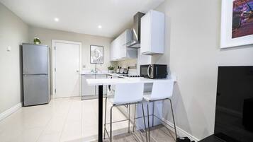 Cocina compacta con encimera blanca, electrodomésticos de acero inoxidable y un taburete de bar.