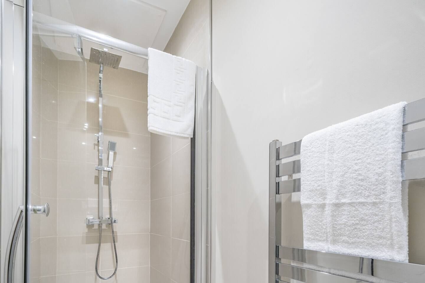 Uma casa de banho moderna com chuveiro envolto em vidro, um porta-toalhas cromado e uma toalha branca pendurada nele.