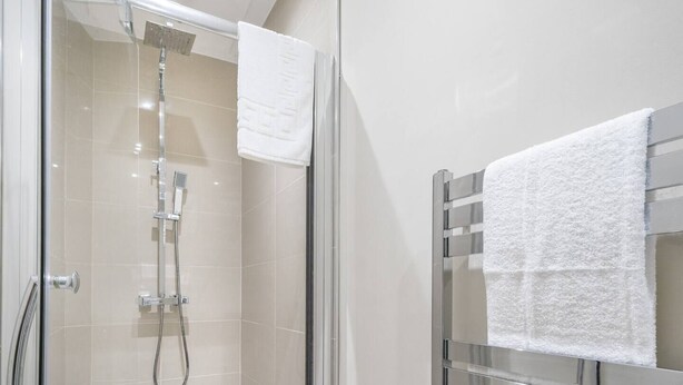 A modern bathroom with a glass-enclosed shower, a chrome towel rack, and a white towel hanging on it.