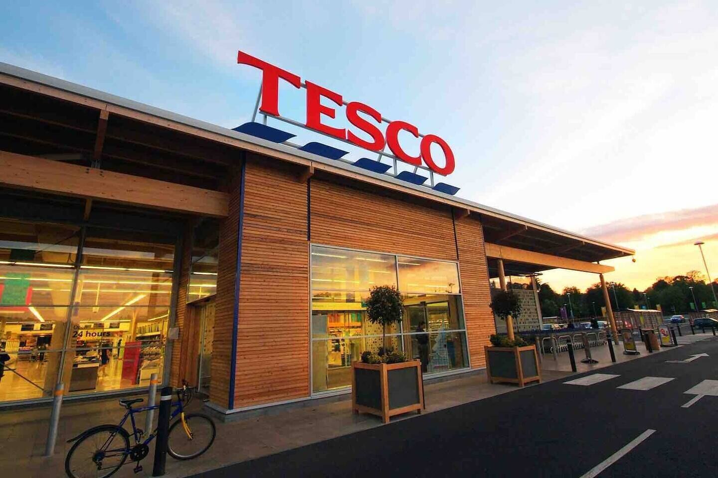 Un magasin Tesco doté d’une façade moderne, de grandes baies vitrées et d’un vélo garé à l’extérieur.