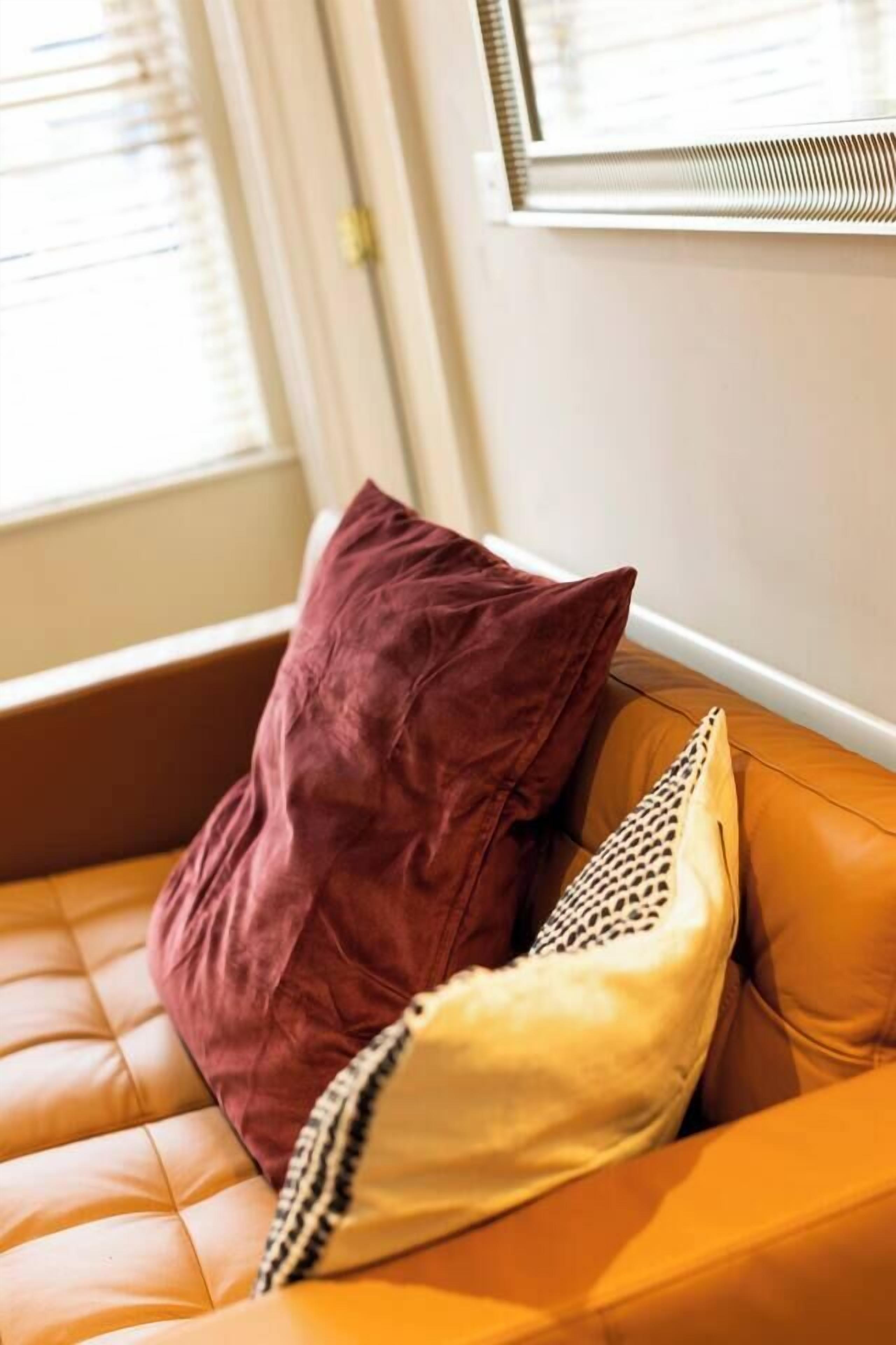 Una habitación con un sofá de cuero marrón, una ventana con persianas y un aire acondicionado instalado en la pared.