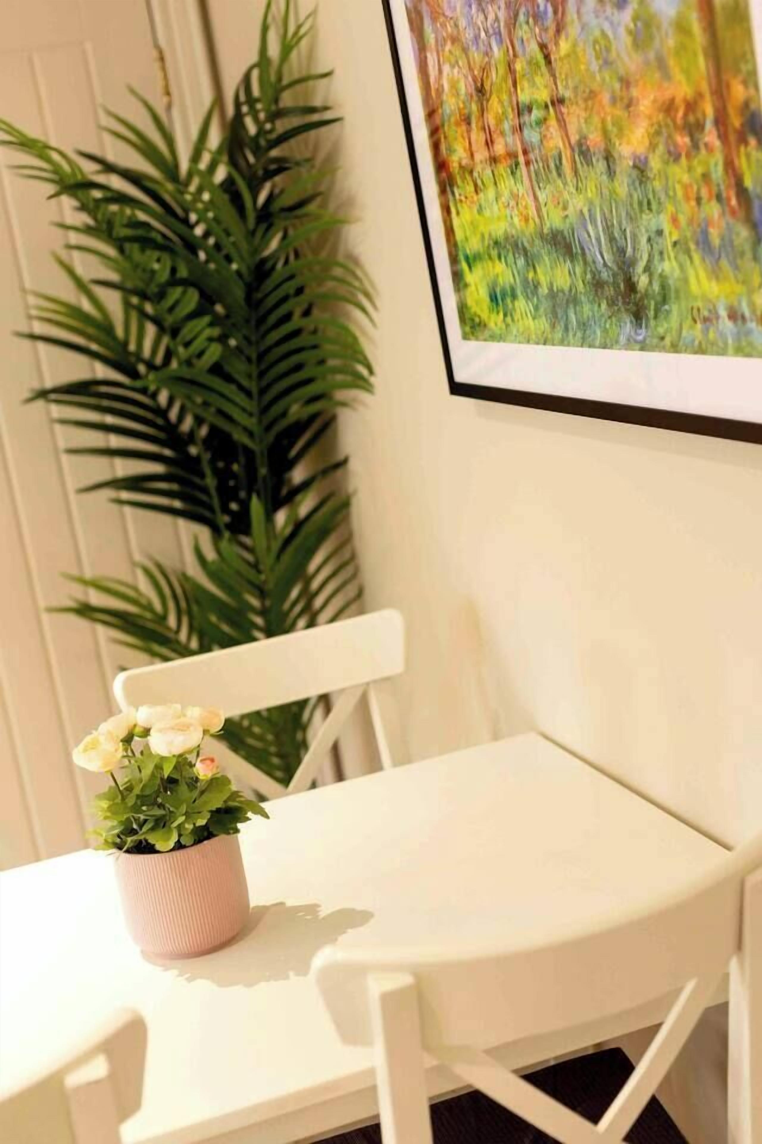 Una mesa de comedor blanca con una planta en maceta y un cuadro en la pared.