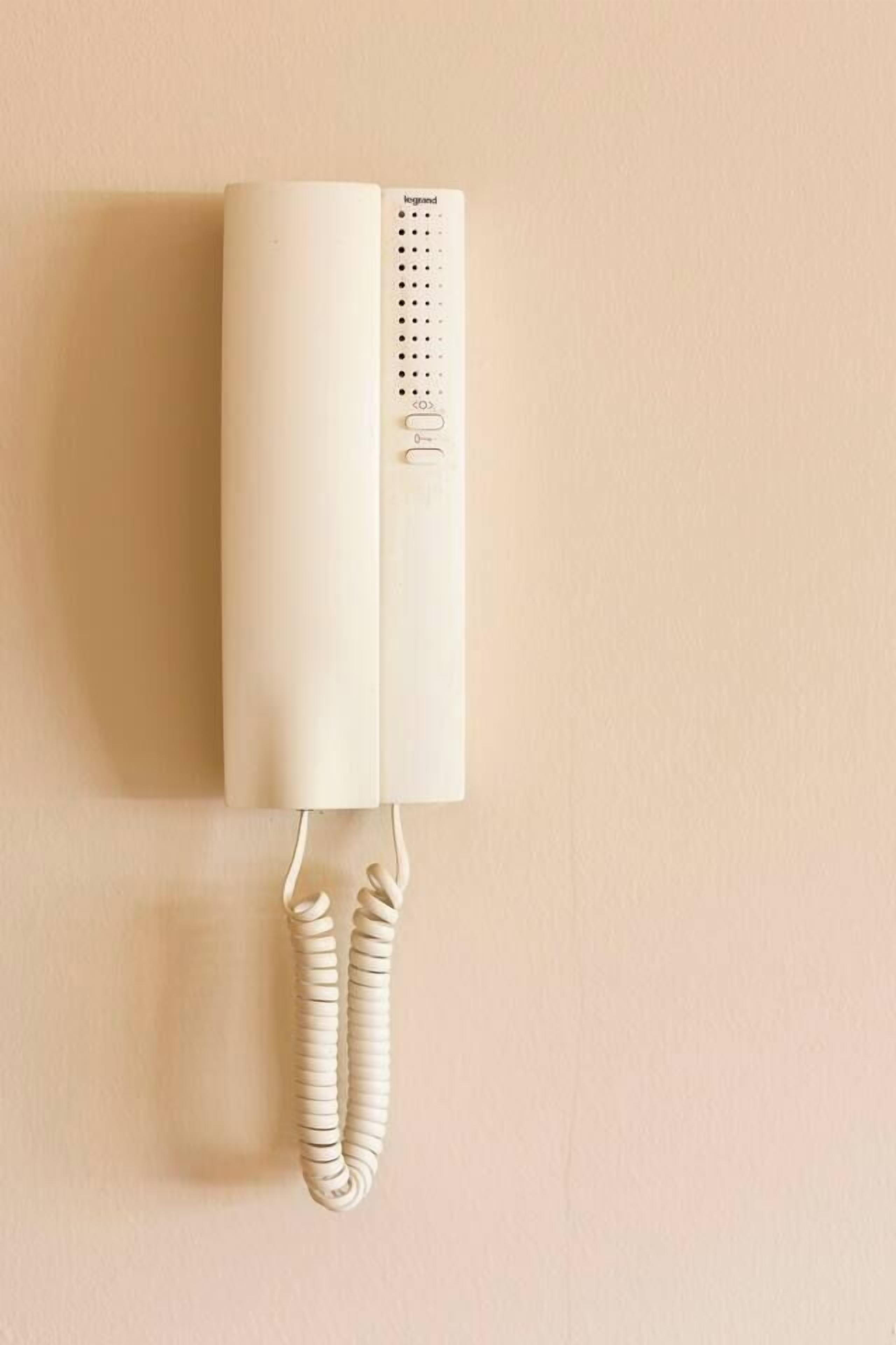 Een aan de muur bevestigd telefoonapparaat met een snoertelefoon.