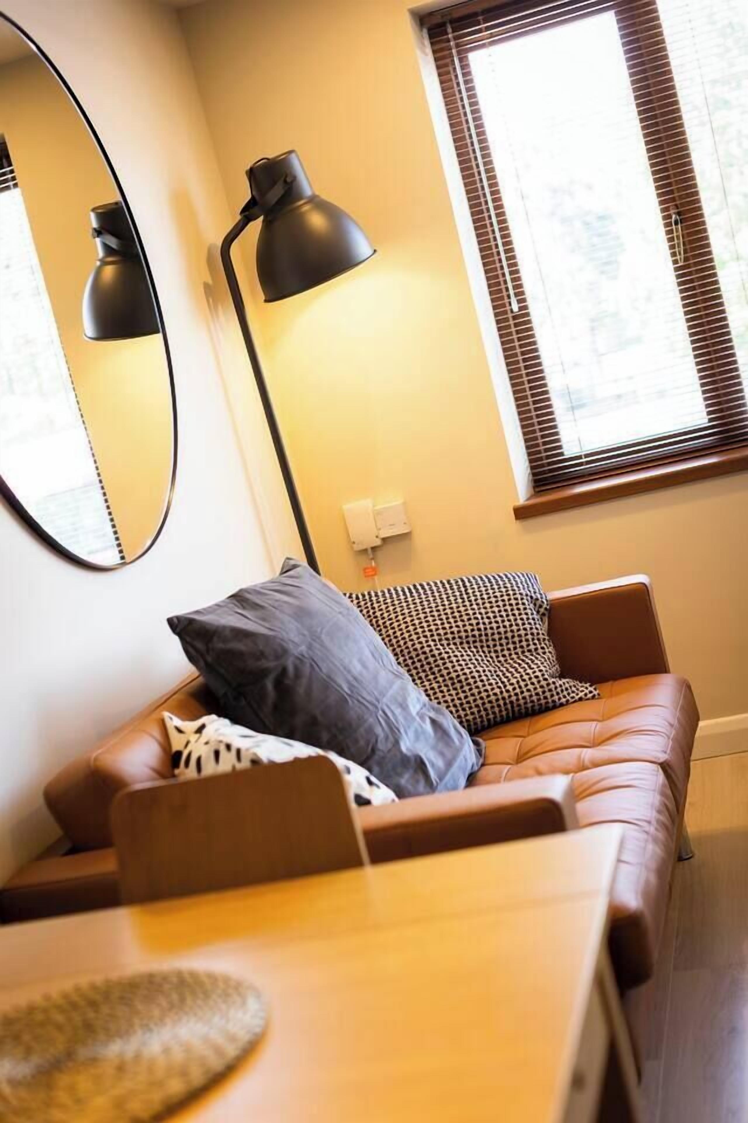 Ein gemütlicher Wohnbereich mit einem braunen Ledersofa, einem Holztisch und einem großen Spiegel an der Wand.