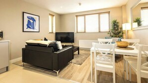 Een moderne woonkamer met een zwarte bank, een witte eettafel en een flatscreen televisie.