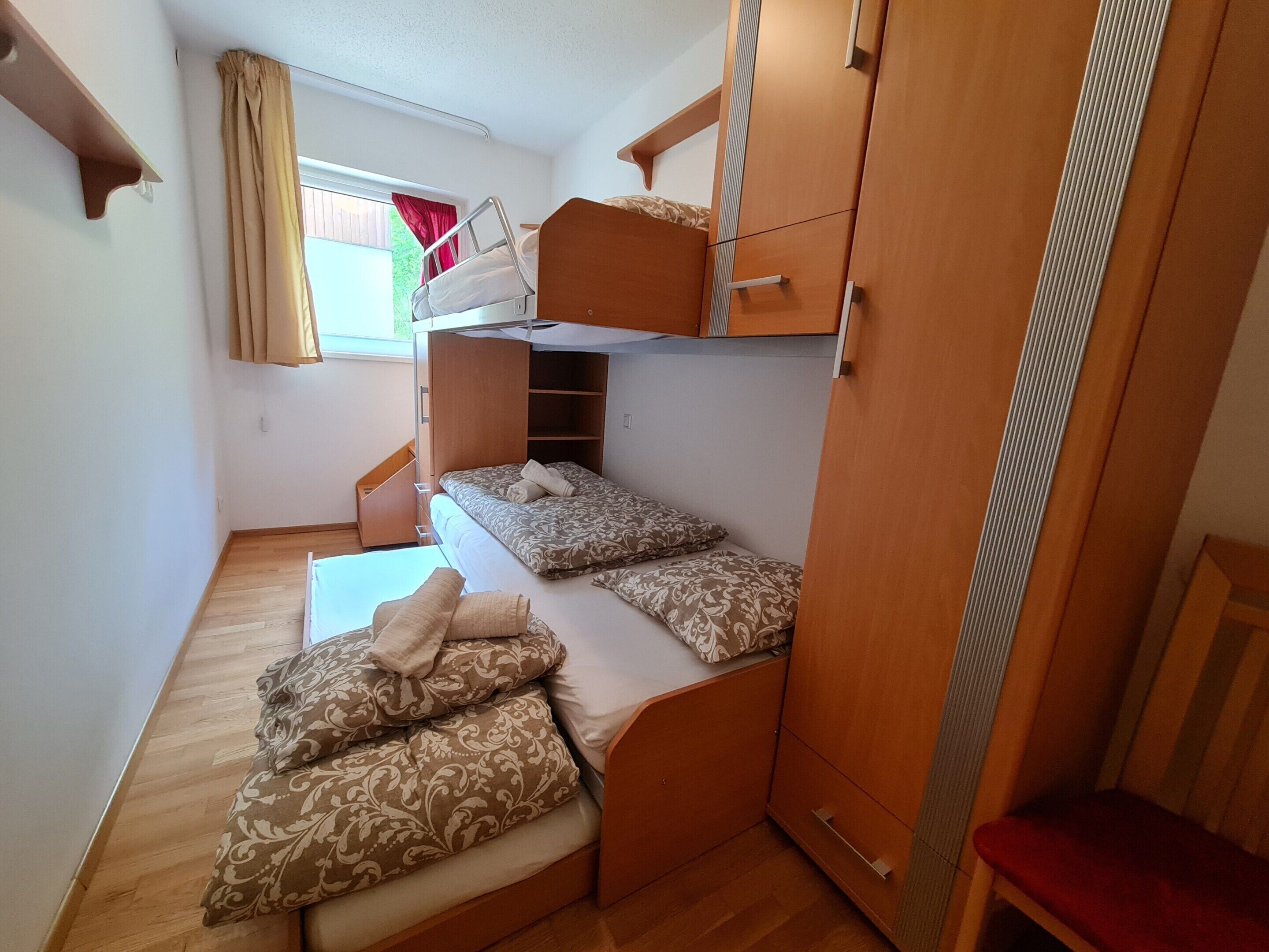 A compact room with bunk beds, a small desk, and a wardrobe.
