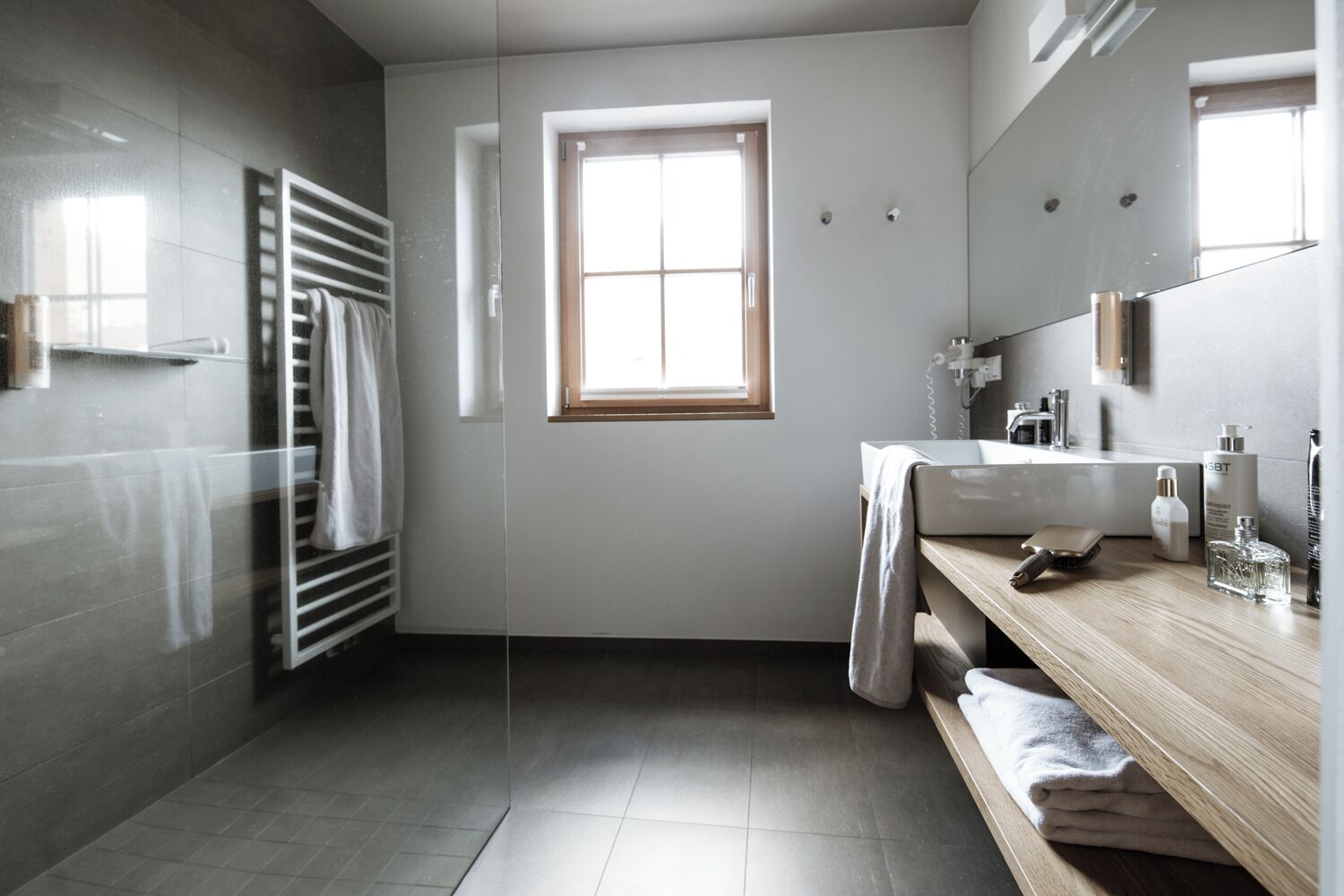 A modern bathroom with a large window, a wooden vanity, and a towel rack.