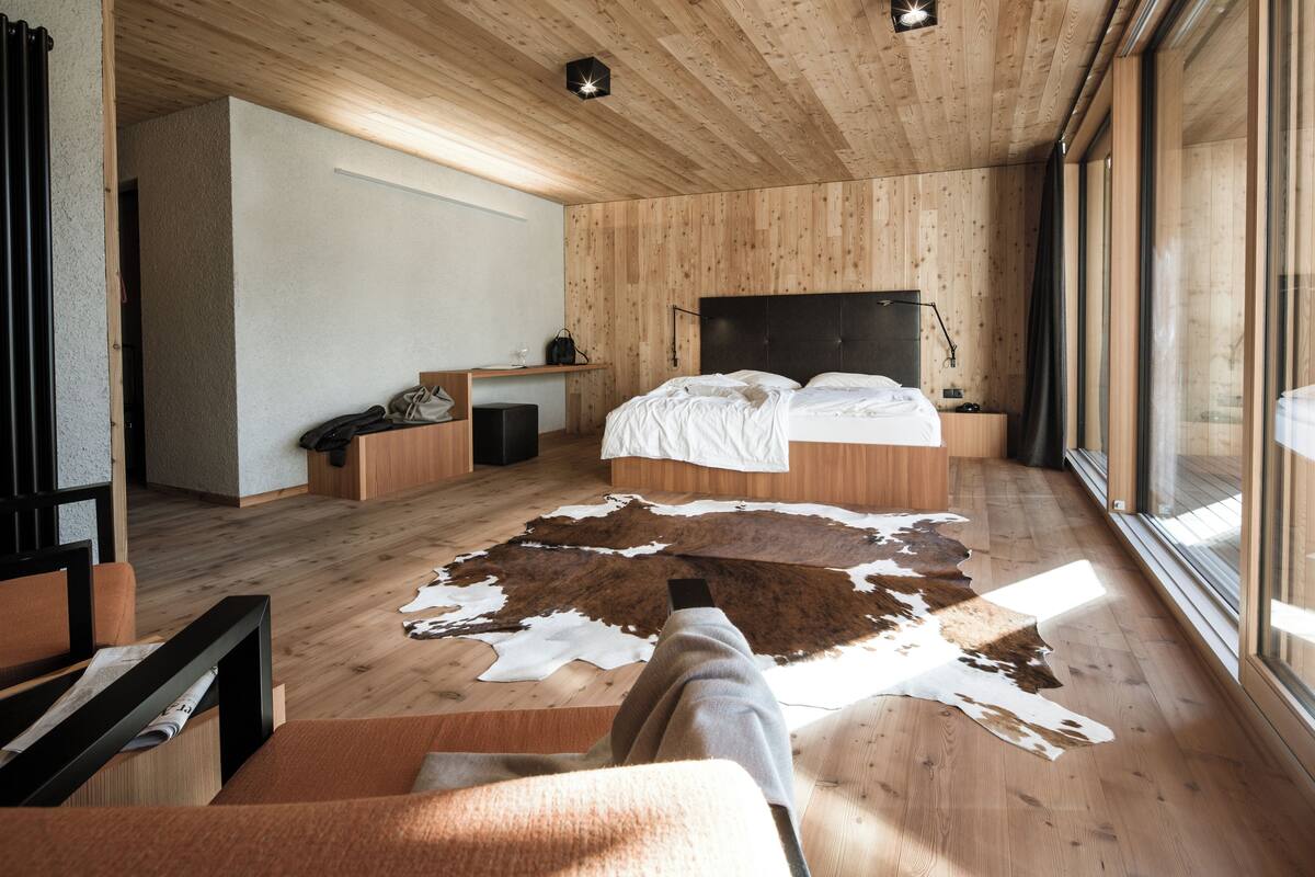 Un dormitorio moderno con techo de madera, una cama grande, un escritorio y un tapete de cuero de vaca.