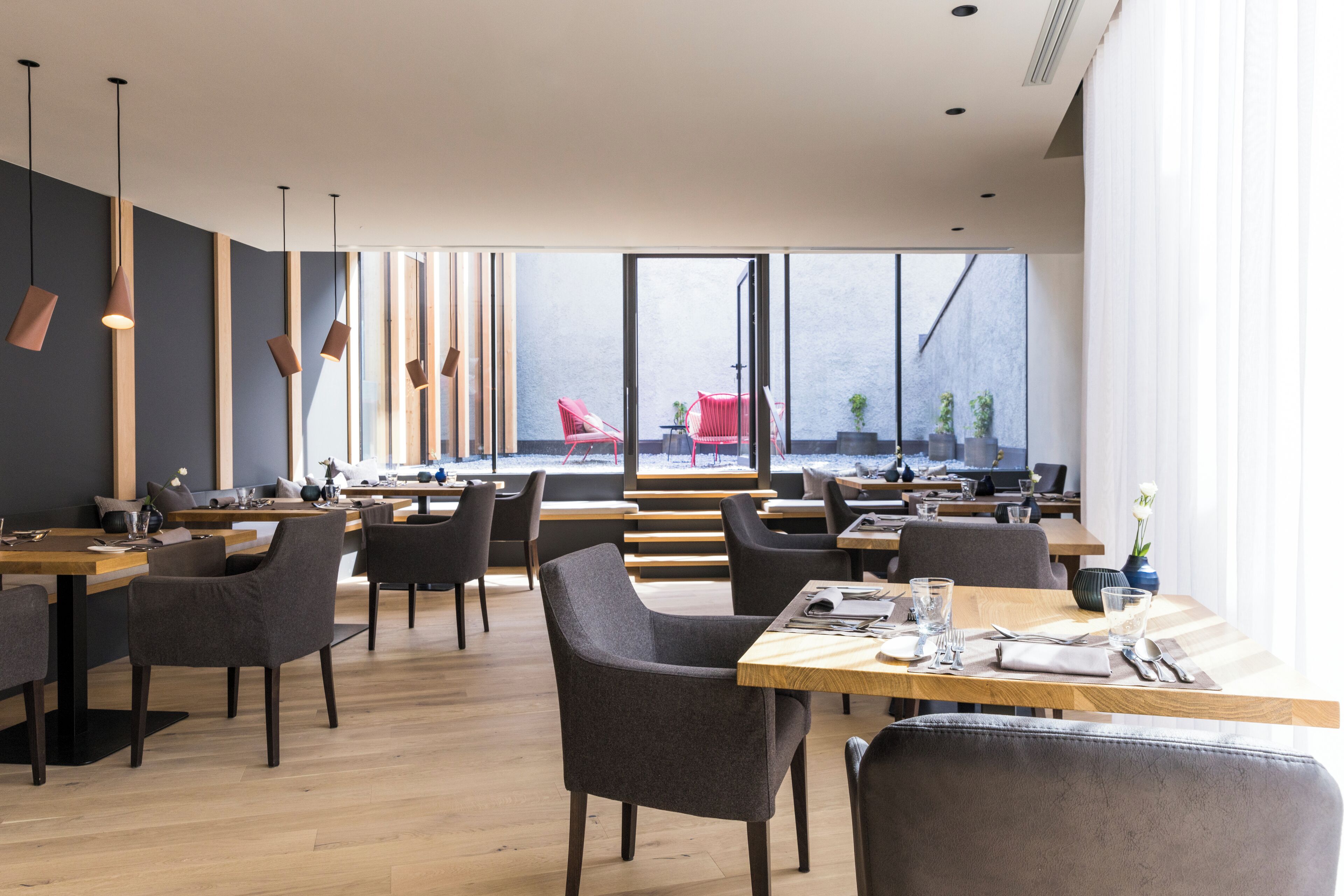 A modern restaurant with wooden tables and chairs, large windows, and pendant lighting.