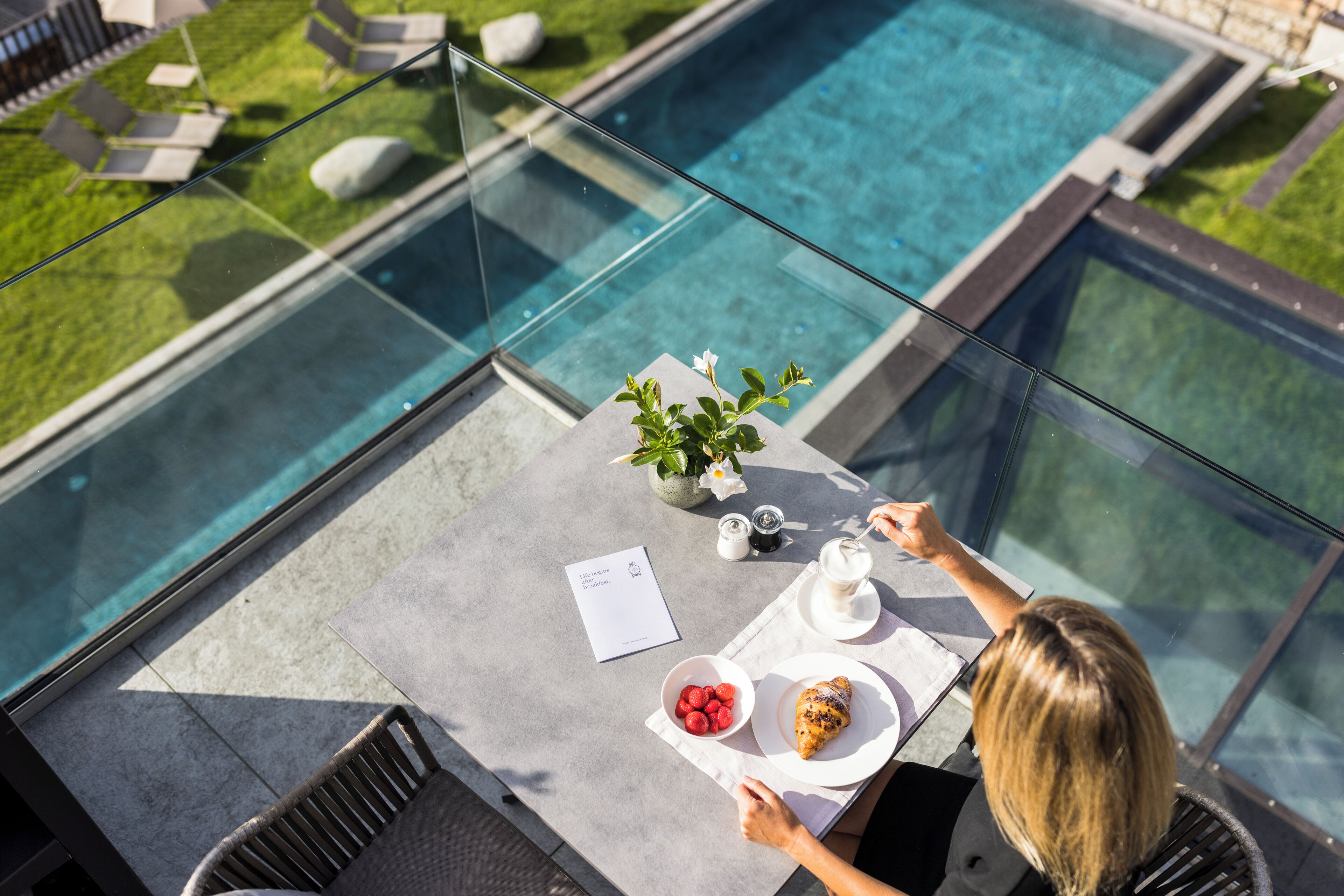 A glass table with a view of a pool, a plant, and a plate with food.