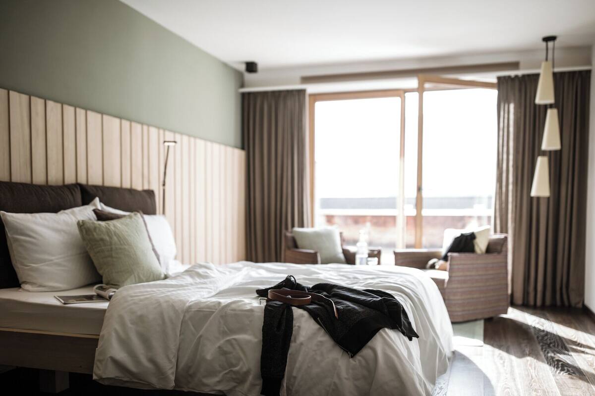Habitación de hotel con cama, una silla, una mesita y vistas al exterior.