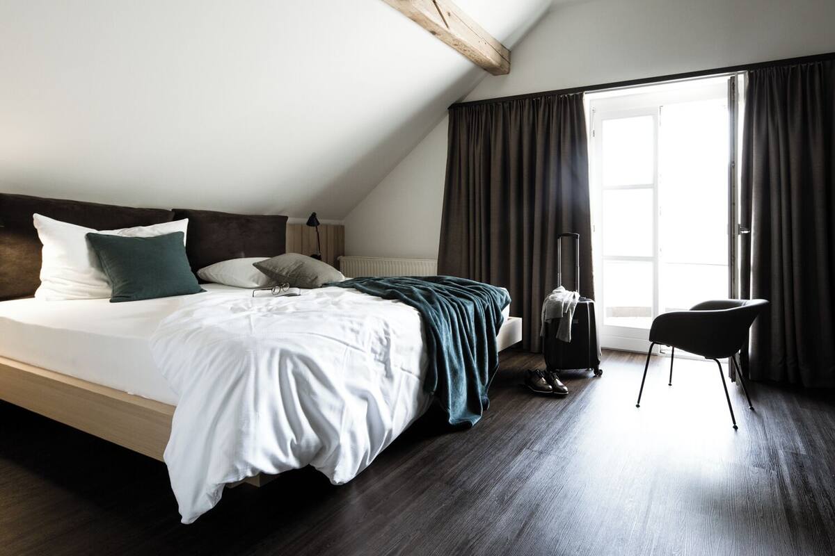 Una habitación de hotel moderna con una cama grande, una maleta y una silla.