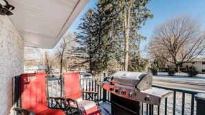 Un espacio al aire libre techado con una parrilla, sillas rojas y vistas a árboles y casas.
