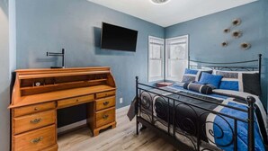 Un dormitorio con cama, un escritorio de madera, un televisor de pantalla plana y decoración mural.