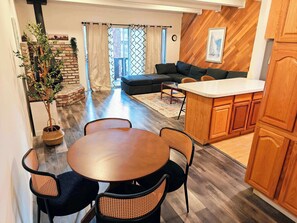 A modern kitchen with wooden cabinets, a dining area with a round table and chairs, a built-in sofa, and a potted plant.