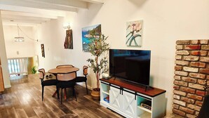 A living room with a TV, a dining table, chairs, a potted plant, and a brick fireplace. - Cozy 3-Bedroom Condo by the Lake & Skiing (Incline Village)