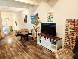Una sala de estar con televisión, una mesa de comedor, sillas, una planta en maceta y una chimenea de ladrillo.