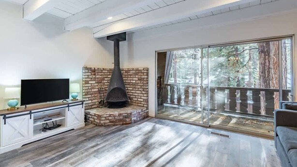 A modern living room with a fireplace, a television, and a sliding glass door leading to a balcony. - Cozy 3-Bedroom Condo by the Lake & Skiing (Incline Village)