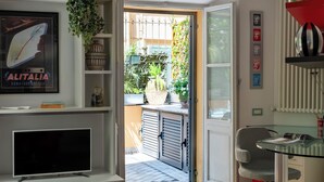 A modern living room with a flat-screen TV, a glass coffee table, and a red sofa. There is a bookshelf with various items and a door leading to an outdoor area with plants. - Terrace Downtown Appartment (Roma)