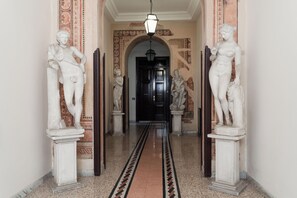A hallway with classical statues flanking the sides, a patterned carpet, and a dark door at the end. - Downtown Apartment with Terrace (Roma)