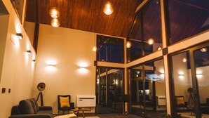 An interior with a sofa, a lamp, a small table, and a large window. - Cabanas do Pico / 2A (Canto da Areia)