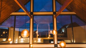A modern interior with large windows, wooden beams, and hanging spherical light fixtures. - Cabanas do Pico / 2A (Canto da Areia)