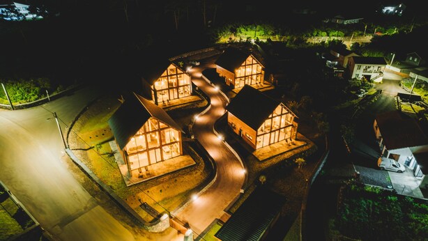 A complex of interconnected buildings with multiple windows, a winding road, and surrounding greenery. - Cabanas do Pico / 2A (Canto da Areia)