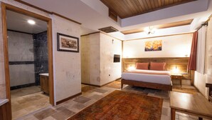 A bedroom with a bed, a nightstand, a wooden bench, a rug, and a shower area. - Unique Cappadocia Palace (Nevsehir)