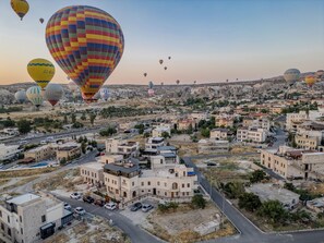 A cityscape with multiple hot air balloons in the sky and a variety of buildings, including a prominent white building with a dome. - Unique Cappadocia Palace (Nevsehir)