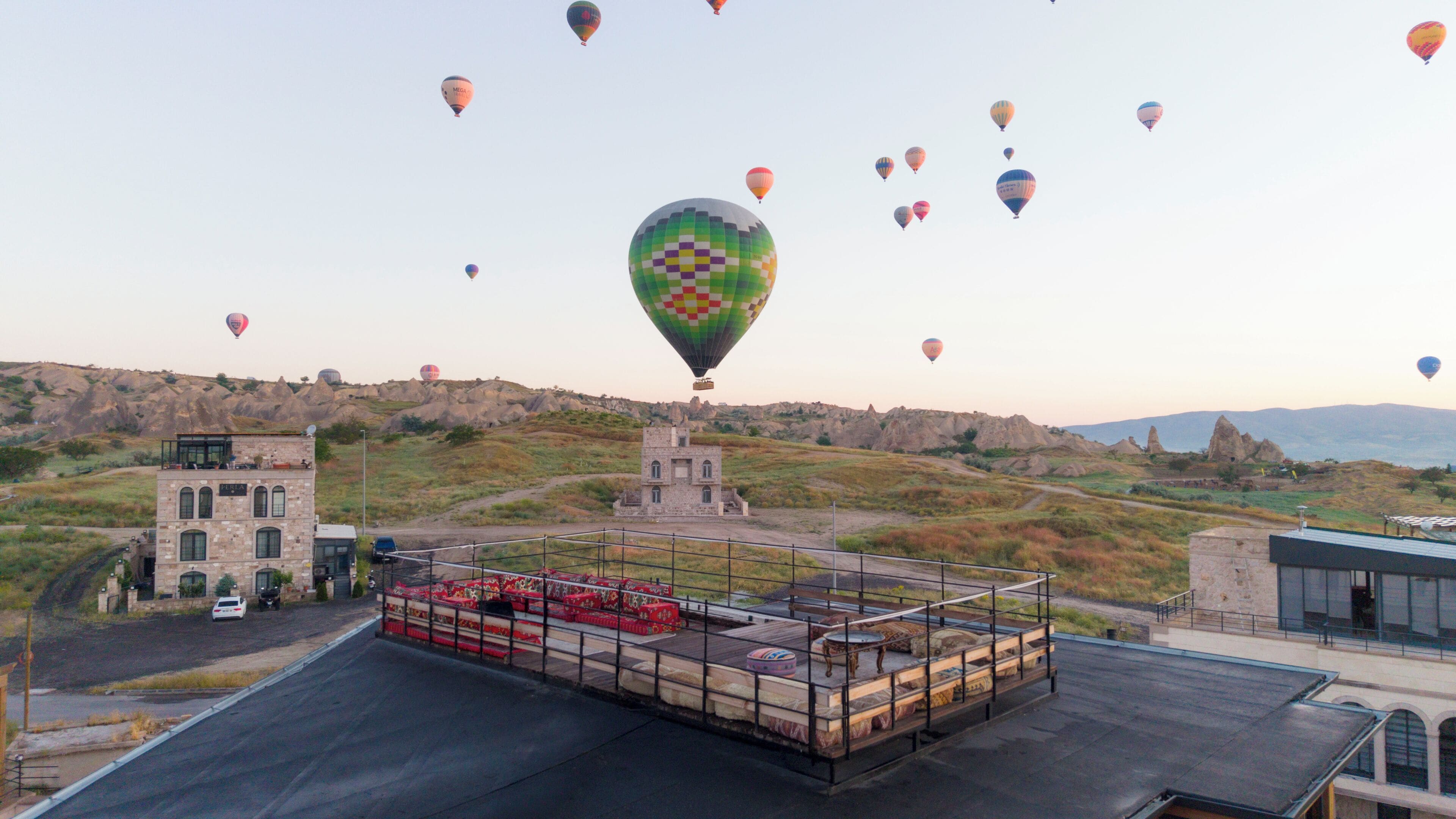 A hot air balloon festival with multiple balloons, a viewing platform with seating, and a backdrop of rocky hills.