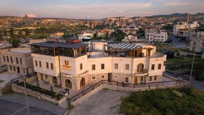 A multi-story building with a prominent 'UNIQUE' sign, featuring a courtyard with outdoor seating and a view of the surrounding cityscape and mountains. - Unique Cappadocia Palace (Nevsehir)