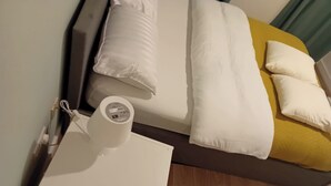 En seng med hvide sengetøj, en gul pude og en hvid pude på et trægulv.