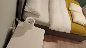 A bed with white bedding, a yellow pillow, and a white pillow on a wooden floor.