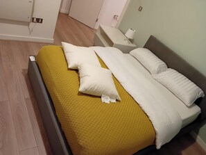 A neatly made bed with a yellow blanket and white pillows, a bedside table with a lamp, and a wooden floor. - 3 Bed-sleeps 6-city Centre-free Parking (Manchester)
