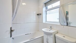 A bathroom with a bathtub, a sink, and a toilet. There is a window with a curtain, and a towel rack is visible. - Host Stay Shaftsbury (Nottingham)