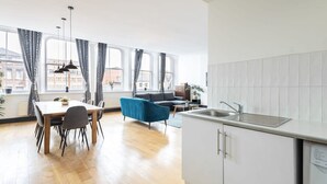 A modern kitchen with white cabinets, a sink, and a dining area with a table and chairs. - Host Stay Exchange Street Living (Liverpool)